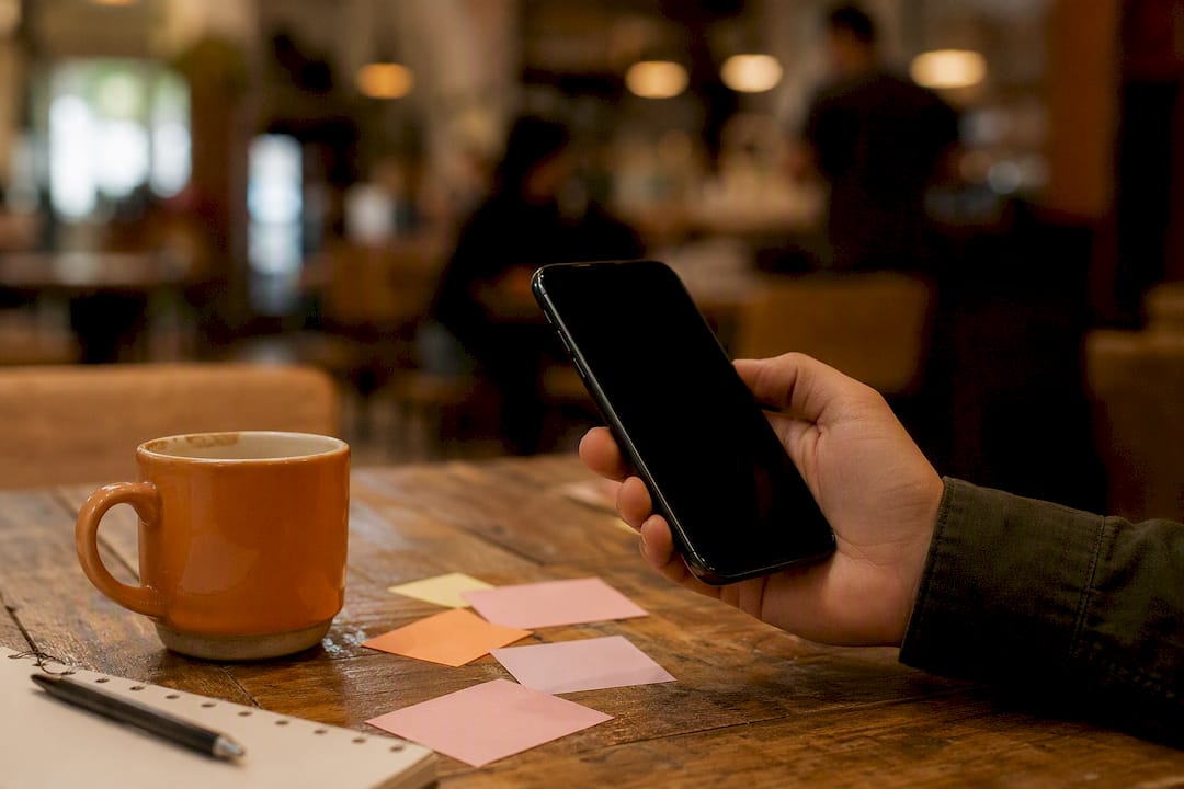 Hand holding smartphone over map and coffee cup